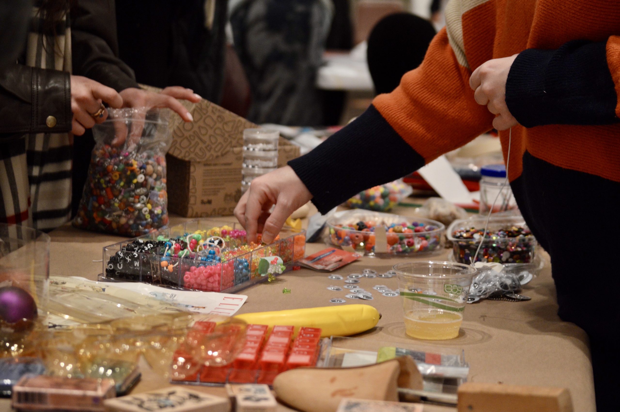 hand grabbing beads on table full of miscellaneous art supplies